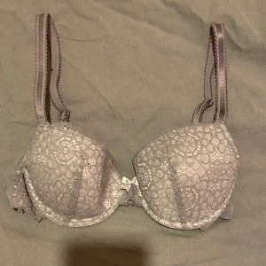 Grå spets-bh med rosett - Säljer en elegant grå bh med spetsdetaljer och en söt liten rosett framtill. Bh:n har justerbara axelband och hakknäppning bak för bästa passform. Perfekt för att känna sig både bekväm och stilren. Pris kan diskuteras!