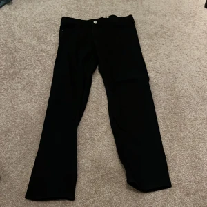 Svarta byxor från H&M - Snygga svarta byxor från H&M i slim fit med justerbar midja. Perfekta för en stilren look. Byxorna har en klassisk design med knappar och dragkedja.