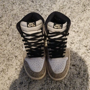 Nike Air Jordan sneakers med svart och grått mönster - Säljer ett par Nike Air Jordan sneakers i vitt, svart och grått med unikt mönster på panelerna. Skorna har högt skaft, svart swoosh och svarta skosnören. Perfekta för dig som gillar streetwear och vill sticka ut.