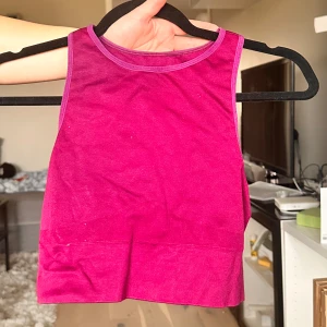 Mörkrosa croppad linnetopp - Säljer en mörkrosa (mer åt lila hållet i verkligheten) croppad linnetopp med rund halsringning. Toppen är ärmlös och har en enkel, sportig design. Perfekt för varma dagar eller som lager under andra plagg.