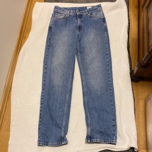 Blå raka jeansbyxor Dobber 38 - Klassiska blå jeansbyxor med normal passform och raka ben. Byxorna har fem fickor, bälteshällor och stängs med dragkedja och knapp. Perfekta till vardags för en avslappnad stil.