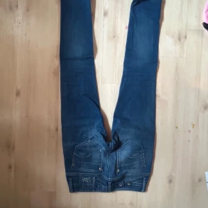 Blå jeans från G-Star - Säljer ett par low waisted blå jeans från trendiga G-Star med snygga slitningar och broderad logga på bakfickan. Skinny jeans och detaljerade sömmar