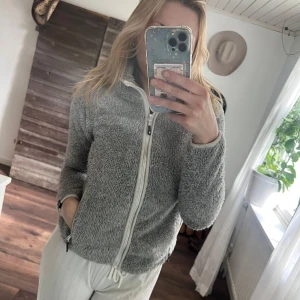 Grå fleece med huva - Mysig grå fleecekofra med huva och vit dragkedja framtill. Perfekt för kyliga dagar när du vill vara både bekväm och varm.