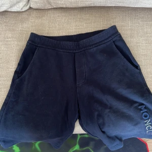 Mörkblå shorts från Moncler - Snygga mörkblå shorts från Moncler med broderad logga på benet och klassisk Moncler-patch baktill. Shortsen har normal passform, två sidofickor och är tillverkade i mjuk bomull. Perfekta för sommardagar när du vill vara både bekväm och stilren.