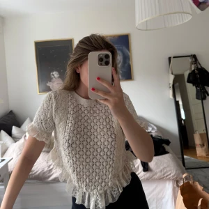 Vit stickad topp med volang och spets  - Säljer en söt vit stickad topp med korta ärmar och volangdetaljer längs nederkanten. Spets nedtill och vid ärmsluten. Perfekt för vår och sommar! Creme vit 