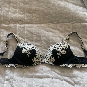 Svart spets-bh med broderade blommor - Säljer en svart bh med vacker vit broderad spets i blommönster då den inte passar mig längre.