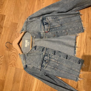 Blå croppad jeansjacka från Levi's - Säljer en blå croppad jeansjacka från Levi's med råa kanter och klassiska bröstfickor. Jackan har knappar framtill och långa ärmar. Perfekt för dig som gillar en trendig och avslappnad stil.