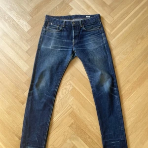 Edwin blå jeans - Klassiska blå Edwin jeans med raka ben och femficksmodell. Jeansen har en brun läderpatch bak i midjan och tydliga slitningar för en cool, använd look. Perfekta för dig som gillar tidlös denimstil.