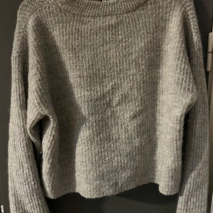 Grå stickad kofta från Gina Tricot - Mysig grå stickad kofta från Gina Tricot med knytband framtill. Koftan har lång ärm och en lite lösare passform, perfekt för lager-på-lager. Enkel och stilren design som passar till mycket. Säljs för 100kr