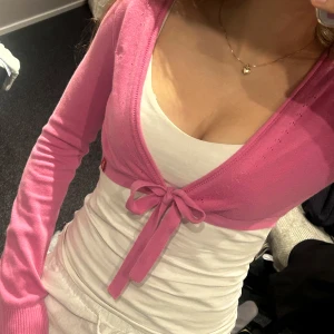 Rosa croppad kofta med knyt - Säljer en söt rosa croppad kofta med knyt framtill. Koftan har långa ärmar och är i ett tunt, mjukt material som passar perfekt över ett linne eller topp. Enkel och stilren design som ger en trendig look.