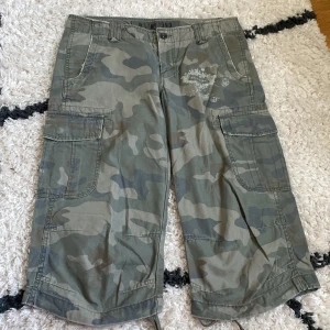 Cargoshorts i camouflage från B Star 1993 - Jätte coola Cargoshorts/jorts i grönt camouflage med flera fickor och tryckdetaljer på ena benet. Säljer då de inte passar mig. Midjemått 41cm rakt över, säljer endast via instabox 