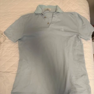 Ljusblå pikétröja från Lanvin - Säljer en ljusblå pikétröja från Lanvin med klassisk krage och två knappar framtill. Tröjan har korta ärmar och en liten broderad logga på bröstet. Perfekt för en stilren och avslappnad look. Nypris ligger på typ 4000 och den är väldigt sällsynt. Steal!