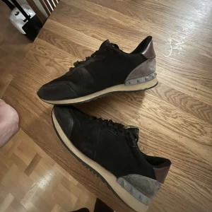 Svarta sneakers med grå och bruna detaljer - Säljer ett par svarta valentino rockruners. Dem är lite slitna men inte så mycket. 