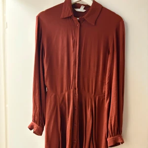 Rostbrun skjortklänning med knappar - Rostbrun skjortklänning med långa ärmar och knappar framtill. Klänningen. 