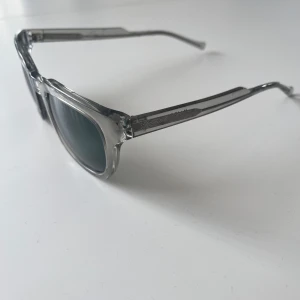 Solglasögon från Kaibosh - Snygga solglasögon från Kaibosh med transparent grå båge och mörka glas. Rektangulär form som ger en modern look. Perfekta för dig som vill sticka ut med stilrena accessoarer😎