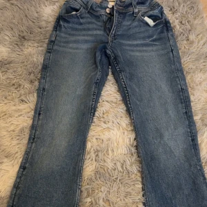 Blå jeans från Gina Tricot - Säljer ett par klassiska blå jeans från Gina Tricot i storlek 170. Jeansen är bootcut, normal passform och snygga detaljer med broderade bakfickor samt dubbla knappar i midjan. Perfekta till vardags och lätta att matcha med olika toppar.