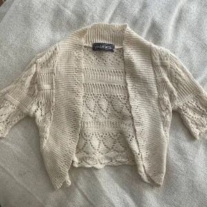 Beige stickad kofta från Quiz - Säljer en söt beige stickad boulero från muizz med korta ärmar och öppet framtill. Koftan har ett virkat mönster och är perfekt att slänga över en topp. Superfin till både jeans och klänning!