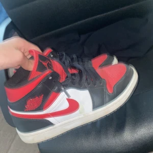 Nike Air Jordan 1 Retro High OG röd/svart/vit - Säljer ett par Nike Air Jordan 1 Retro High OG i klassiska färgerna röd, svart och vit. Skorna har svart snörning, rund tå och platt sula. Perfekta för dig som gillar streetwear och sneakers med ikonisk design.