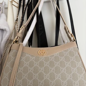 Beige axelväska  - Säljer en beige/ krämfärgad och ljus rosa axelväska med GG-mönster och guldfärgade detaljer. Väskan har dragkedja upptill och justerbar axelrem. Insidan är ljus med ett innerfack. Perfekt för dig som gillar stilrena accessoarer.