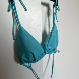 Turkos trekantsbikini med knyt - Säljer en turkos trekantsbikini med knyt i hals och rygg. Klassisk modell med tunna band och enkel design, perfekt för stranden eller poolen. Snygg och stilren färg som passar till sommaren. Från Nelly i stl M. Säljer för att den var fel storlek.  Säljer samma på Vinted så kontakta gärna innan ni trycker på ”köp”!