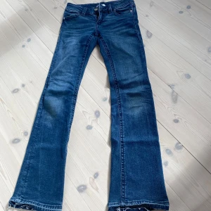 Blå bootcut jeansbyxor - Säljer ett par klassiska blå bootcut jeans med låg midja. Byxorna har fem fickor, dragkedja och knapp framtill samt snygga detaljer på bakfickorna. Perfekta för dig som gillar en tidlös jeansstil.