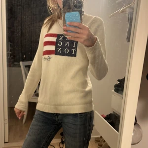 Vit stickad tröja från Lexington - Säljer en vit stickad tröja från Lexington med amerikanskt flaggmotiv och text på bröstet. Tröjan har rund halsringning och långa ärmar. Perfekt för dig som gillar klassisk och stilren design.