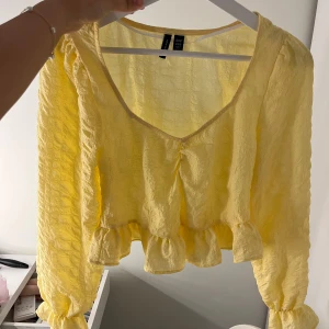 Gul volangblus från Vero Moda - Säljer en söt gul topp från Vero Moda med volangdetaljer nedtill och vid ärmslut. Toppen har v-ringning och långa ärmar. Perfekt för vår och sommar, superfin till både jeans och kjol! Storlek xs bra skick