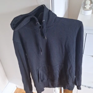 Svart hoodie i storlek L - Säljer en klassisk svart hoodie med huva och känguruficka. Perfekt för en avslappnad stil och enkel att matcha med det mesta. Mjuk och bekväm med dragsko i huvan.