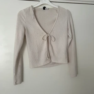 Vit ribbad croppad topp med knyt - Säljer en vit ribbad croppad topp med v-ringning och knyt framtill. Toppen har långa ärmar och är perfekt för att skapa en stilren och trendig look.