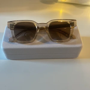 Beige solglasögon från CHIMI  - Snygga solglasögon med transparent beige båge och bruna glas. Rektangulär form som ger en modern look. Perfekta för soliga dagar och passar till många stilar. Kommer med ett stilrent fodral.