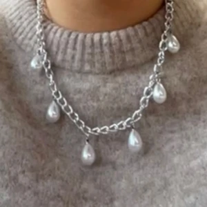 Silverfärgat halsband med pärldroppar - Säljer ett trendigt halsband i silverfärgad kedja med flera hängande droppformade pärlor. Perfekt för att lyfta vilken outfit som helst med en cool och elegant touch.