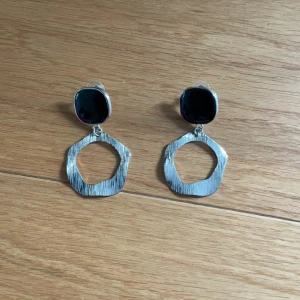 Silvriga statement örhängen med oregelbunden form - Säljer ett par coola silvriga örhängen med oregelbunden, modern design. Örhängena har två delar: en platt, rundad topp och en större, vågig cirkel som hänger nedanför. Perfekta för att lyfta vilken outfit som helst!