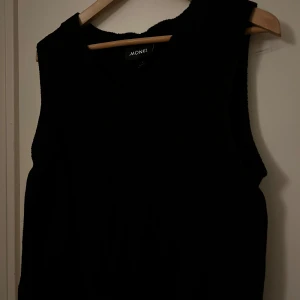 Svart stickad väst från Monki - Svart stickad väst från Monki med v-ringning och diskret kabelstickat mönster framtill. perfekt att styla över en skjorta eller t-shirt.