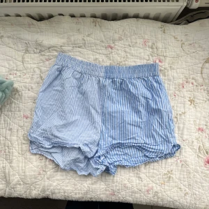Pyjamasshorts - Randiga pyjamasshorts från Gina Tricot💕De har blivit använda några gånger men har inga defekter, de är bara lite skrynkliga. De är blå och vit randiga. Ränderna sitter lite tätare ihop på enda sidan än den andra. På sista bilden kan man se att shortsen har en liten slits☺️