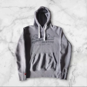 Grå hoodie från Superdry - Säljer en snygg grå hoodie från Superdry! Färgen på tröjan är stentvättad grå vilket gör tröjan sjukt snygg! Passformen på tröjan är slim fit och skicket är bra! Vid fler frågor är det bara att höra av er!