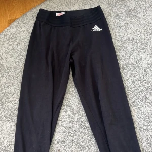 Svarta leggings från Adidas - Svarta leggings från Adidas med vit logga på vänster höft. Byxorna är tillverkade i ett stretchigt material som passar perfekt till träning eller vardag. Klassisk och enkel design.