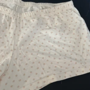 Vita blommiga shorts från Brandy Melville - Säljer ett par vita shorts från Brandy Melville med små blommiga mönster i rosa och orange. De har en elastisk midja och är tillverkade i mjuk bomull, perfekta för varma dagar. Storlek ungefär xs/s passar även m