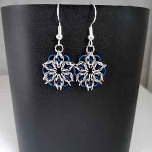 Egentillverkade örhängen  - Egentillverkade örhängen gjorda med bindringar i stålfärgag samt mörkblåa matta ringar. Längd ca 3cm långa. Blomman är ca 2cm lång. Öronkroken är nickelsäker och aldrig använda 