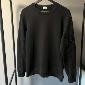 C.P. Company Tröja - Svart C.P. Company sweatshirt, använd sparsamt ett par gånger. Tröjan är köpt på Farfetch, kvitto finns. Tröjan har en liten repa på cp company loggan (bild 2) men det syns knappast. Skriv om du har några frågor!😀