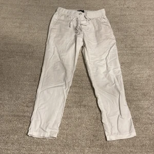 Vita linne byxor från Zara - Säljer ett par vita byxor från Zara med elastisk midja och dragsko. Byxorna har raka ben och är tillverkade i linnen som passar perfekt för varmare dagar. Enkla fickor på sidorna och stilren design.