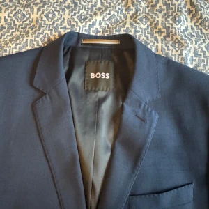 Mörkblå kostym från BOSS - Säljer en stilren mörkblå kostym från BOSS med italienskt tyg från Marzotto. Kavajen har två knappar, klassiska slag och fickor med lock. Byxorna är raka och dressade. Perfekt till studenten! Storleken är M(EU48)