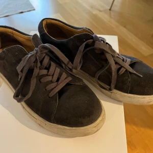 Myrqvist Grå mockasneakers med snörning - Säljer ett par svarta sneakers i mocka med klassisk rund tå och platt vit sula. Skorna har snörning och en stilren design som passar till det mesta. Perfekta för dig som gillar en enkel och tidlös look.