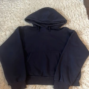 Svart hoodie från Gina Tricot - En svart hoodie från Gina Tricot med huva och magficka. Tröjan har långa ärmar, ribbade muddar och en klassisk passform. Perfekt för en avslappnad stil. Den är lite sönder vid halsen men det är inget man tänker på!