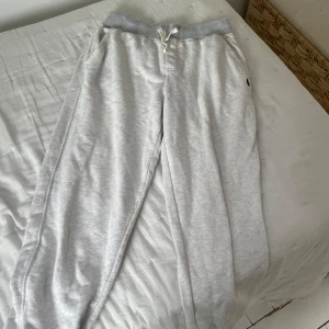 Grå mjukisbyxor från Polo Ralph Lauren - Snygga ljusgrå mjukisbyxor från Polo Ralph Lauren med mörkblå logga broderad på benet. Byxorna har dragsko i midjan och muddar i grått upptill. Perfekta för en avslappnad stil.