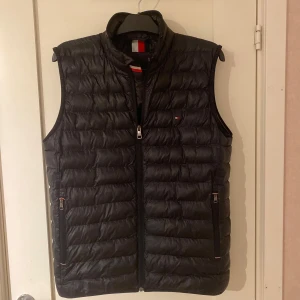 Tommy Hilfiger väst - Säljer min väst då den inte kommer till användning för den va för stor. Väldigt bra skick. Modellen på bilden är 177 och väger cirka 62kg. Den är 67cm om man mäter från axlarna och neråt och 54 cm på midjan priset kan diskuteras 