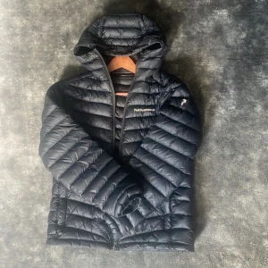 Svart dunjacka med huva från Peak Performance - Säljer en svart dunjacka från Peak Performance i storlek S. Jackan har huva, dragkedja framtill och är quiltad för extra värme. Perfekt för kyliga dagar och enkel att matcha med olika outfits.