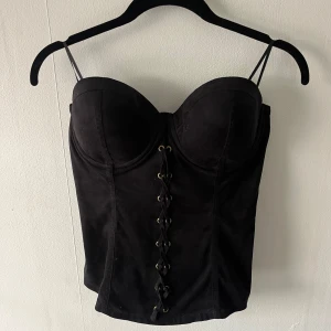 Svart korsettopp från Guess - Korsettopp från Guess, snörrerna är bara dom man hänger upp på galgar med, inga axelband. Perfekt för att skapa en snygg och edgy look. Skulle säga att det mer är storlek M🫶🏼