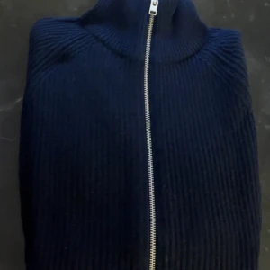 Mörkblå ribbad zip-tröja från Jack&Jones - Mörkblå ribbstickad tröja med dragkedja hela vägen och hög krage. Jackan har lång ärm. Perfekt för lager-på-lager och enkel att matcha. Inte kommit till användning och säljer därför. Använd knappt fåtal gånger. Skriv för frågor!