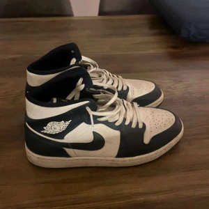 Nike Air Jordans 1s - Säljer ett par klassiska Nike Air Jordans i svart och vitt. Skorna har högt skaft, vit bas med svarta detaljer och snörning framtill. Perfekta för dig som gillar streetwear och vill ha en ikonisk sneaker i garderoben. Priset kan diskutera 