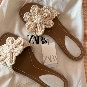 Sandaler - Säljer ett par superfina sandaler från Zara, helt oanvända med lapp kvar, med virkad blomma upptill. De är beige med bruna sulor och har öppen tå. Perfekta för sommaren 💘💘💘🍒💛
